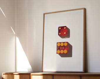 Op de afbeelding: Ingelijste kunstdruk met twee rode dobbelstenen met gele stippen en het nummer 262. De dobbelstenen staan tegen een witte achtergrond in een houten lijst. Het kunstwerk wordt tentoongesteld op een houten kast, met schaduwen van zonlicht.