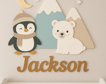 May include: A nursery wall decor set featuring a penguin wearing a hat and scarf, a polar bear, two mountains, snowflakes, and a crescent moon. The name "Jackson" is displayed in wooden letters below the animals. The decor is designed in a neutral color palette.