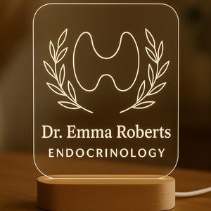 May include: A light-up acrylic sign with a wooden base. The sign displays the name "Dr. Emma Roberts" and the word "ENDOCRINOLOGY" in white text. A medical symbol is centered above the name, with laurel branches on either side.