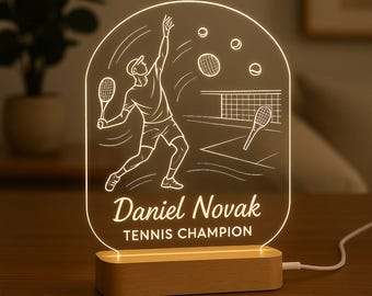 May include: A tennis-themed night light with a wooden base. The clear acrylic panel features a line drawing of a tennis player serving, tennis balls, and a net. The name "Daniel Novak" and "TENNIS CHAMPION" are printed below the illustration.