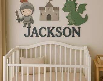 May include: A nursery wall decor set featuring a knight, castle, and dragon in shades of gray and green. The name "JACKSON" is displayed below the figures. A white crib with a beige mattress is in the foreground.