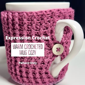 Peut inclure: Un chauffe-tasse en crochet rose avec un bouton sur le côté. Le chauffe-tasse est sur une tasse blanche. Le texte "Expression Crochet" et "Warm Crocheted Mug Cozy" est sur le chauffe-tasse. Le texte "Pattern Only" est également sur le chauffe-tasse.