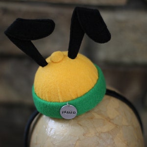May include: A yellow and green headband with black felt ears and a silver charm that says "Pluto".