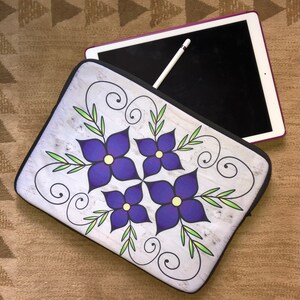 May include: A white laptop sleeve with a floral design featuring four purple flowers with yellow centers and green leaves. The flowers are arranged in a symmetrical pattern and are surrounded by black swirls. The sleeve is made of a soft, durable material and is perfect for protecting your laptop.