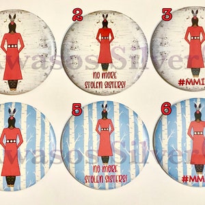 以下が含まれることがあります： 白地に青と白の白樺の木の模様が描かれた丸いボタンが6つあります。ボタンには、赤いドレスを着た頭飾りをつけた女性が描かれています。ボタンには「No More Stolen Sisters!」と「#MMIW」の文字が書かれています。