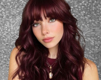 May include: A person with long, wavy, burgundy-colored hair with bangs. The person has fair skin, green eyes, and is wearing a burgundy top and a necklace with a pendant. The background is a textured gray.