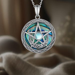 Puede incluir: Collar con colgante de plata con un diseño circular y una estrella de cinco puntas. El colgante tiene un fondo iridiscente de concha de abulón y una pequeña piedra redonda de color azul claro en el centro de la estrella. Cadena de plata.