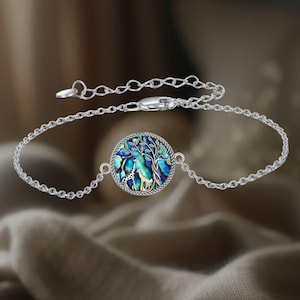 May include: A silver chain bracelet with a round pendant featuring a blue and green abalone shell with a silver tree and giraffe design.