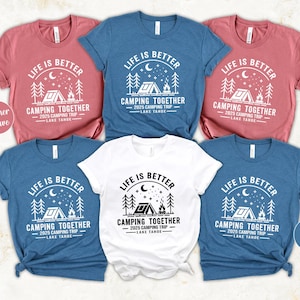 May include: A collection of short-sleeved t-shirts in various colors, including heather mauve, deep teal, and white. Each shirt features a camping-themed graphic with the text "LIFE IS BETTER CAMPING TOGETHER 2025 CAMPING TRIP LAKE TAHOE."
