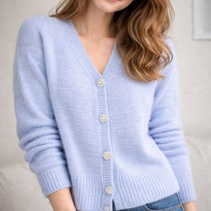 May include: A light blue cardigan with a V-neck and long sleeves. The cardigan has four decorative, round, jeweled buttons down the front. The cardigan is paired with blue jeans.