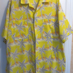 May include: Yellow button-down shirt with a tropical palm tree pattern. The shirt features short sleeves, two chest pockets, and a classic collar. The palm trees are gray, with orange and yellow accents.