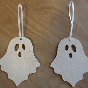 May include: Two ghost-shaped ornaments with a light beige color and glitter accents. Each has a white ribbon for hanging and three oval cutouts for eyes and mouth. Perfect for Halloween decorations.