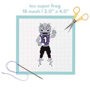 Puede incluir: Un proyecto de punto de cruz con la mascota TCU Super Frog, que lleva una camiseta morada con el número 1. El diseño está sobre tela de 18 mallas, midiendo 5,08 cm x 10,16 cm. Incluye tijeras y una aguja con hilo morado.