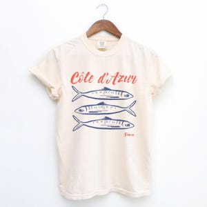 Ivory Beige T-shirt with the text Côtes d'Azur, France.

Côtes d'Azur France T-Shirt, Old Money Aesthetic, 3 Fish , French Riviera, Heritage, Sardines TShirt, France Travel Tee, Coastal Aesthetic, Retro Graphic Tee, French Vacation, Mediterranean