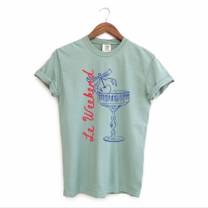 Bay Green T-shirt with the text Le Weekend and a Cherry Coquette Cocktail graphic.

Because what’s a good time without a little flair?

Perfect for brunch dates, rooftop soirées, or just channeling that effortlessly flirty energy. French twist, retro feel, full-on main character mood.
Weekend Shirt, Le Weekend, French T-Shirt, Weekending, Vintage Aesthetic, Coquette Bow Cherry, Cocktail Tee, y2k T-shirt, weekend vibes tee.