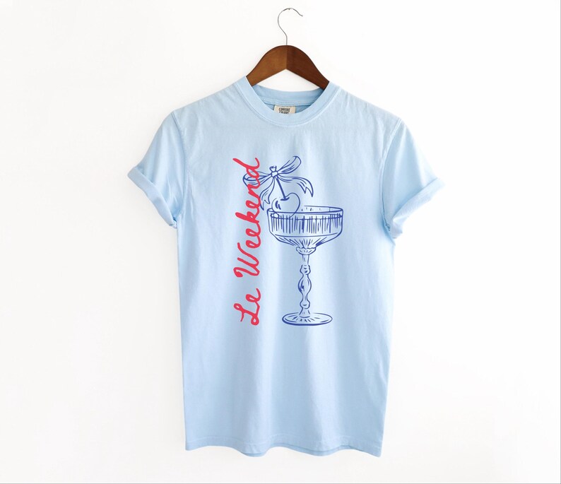 Chambray Light Blue T-shirt with the text Le Weekend and a Cherry Coquette Cocktail graphic.

Because what’s a good time without a little flair?

Perfect for brunch dates, rooftop soirées, or just channeling that effortlessly flirty energy. French twist, retro feel, full-on main character mood.
Weekend Shirt, Le Weekend, French T-Shirt, Weekending, Vintage Aesthetic, Coquette Bow Cherry, Cocktail Tee, y2k T-shirt, weekend vibes tee.