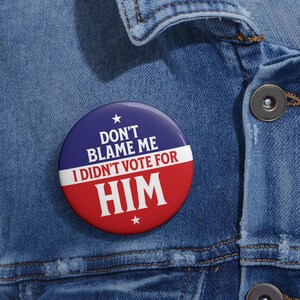 May include: A red, white and blue button with the text "Don't Blame Me I Didn't Vote For HIM" on a denim jacket.