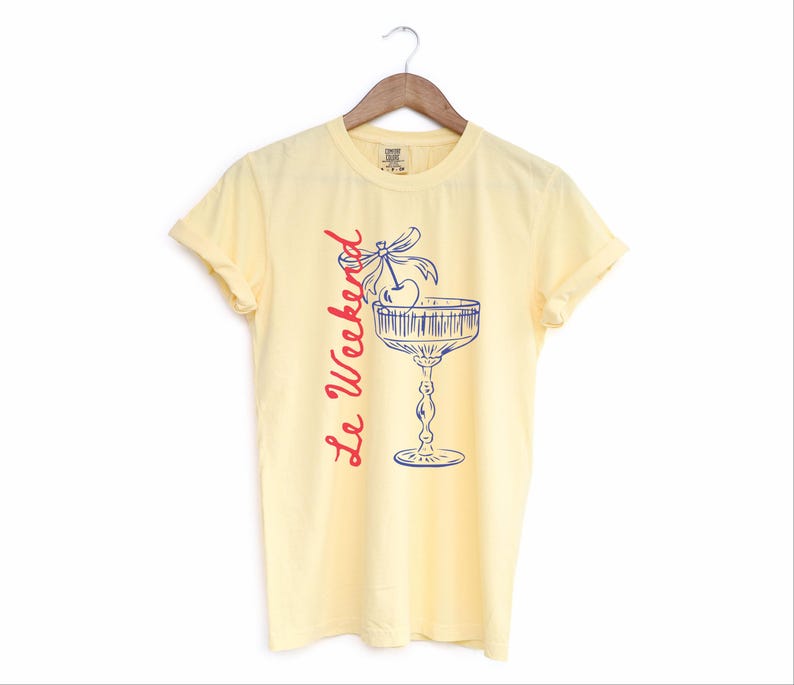 Butter Yellow T-shirt with the text Le Weekend and a Cherry Coquette Cocktail graphic.

Because what’s a good time without a little flair?

Perfect for brunch dates, rooftop soirées, or just channeling that effortlessly flirty energy. French twist, retro feel, full-on main character mood.
Weekend Shirt, Le Weekend, French T-Shirt, Weekending, Vintage Aesthetic, Coquette Bow Cherry, Cocktail Tee, y2k T-shirt, weekend vibes tee.