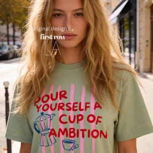 Woman wearing Dolly Parton "Pour Yourself a Cup of Ambition" Shirt, Retro Coffee Graphic, 9 to 5 Country Music Tee, Moka Pot, Coffee Club, Caffeine Lover.

Original desgin and copyright by first row LA.