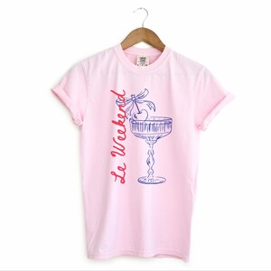 Blossom Pink T-shirt with the text Le Weekend and a Cherry Coquette Cocktail graphic.

Because what’s a good time without a little flair?

Perfect for brunch dates, rooftop soirées, or just channeling that effortlessly flirty energy. French twist, retro feel, full-on main character mood.
Weekend Shirt, Le Weekend, French T-Shirt, Weekending, Vintage Aesthetic, Coquette Bow Cherry, Cocktail Tee, y2k T-shirt, weekend vibes tee.