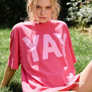Woman wearing YAY T-Shirt, Happy Pink Graphic Tee, Cute Positive Shirt, Feel Good Tee, Fun Handwritten Statement Shirt, Dopamine shirt.

Original design and copyright by first row LA 2026.