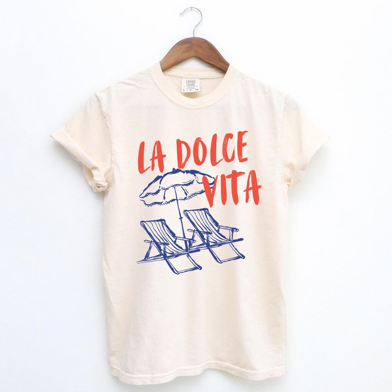 Ivory Beige Model tee with the text LA DOLCE VITA across the chest.
Two sun chairs. One umbrella. Zero worries. Italy -where the espresso hits hard, the gelato never melts, and responsibility? Never heard of her.
Endless summer, featuring a dreamy graphic of striped beach bliss. Perfect for sun-chasers, rule-breakers, and anyone who believes naps are a lifestyle.
La Dolce Vita shirt, Tomato Girl summer, Limoncello, spaghetti vibes. Retro foodie, Portofino, Amalfi Coast Shirt, Sardines Tee