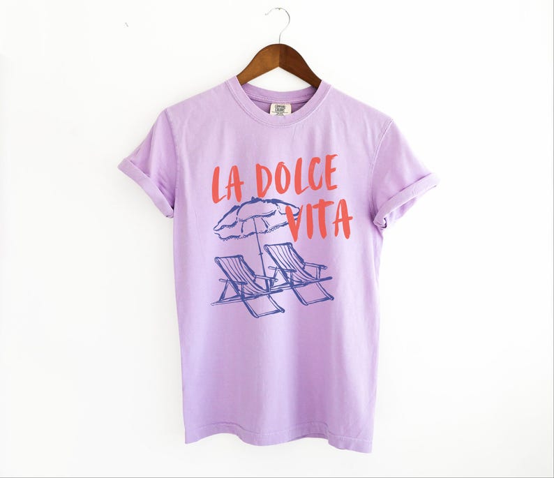 Orchid Purple Tee with the text LA DOLCE VITA across the chest.
Two sun chairs. One umbrella. Zero worries. Italy -where the espresso hits hard, the gelato never melts, and responsibility? Never heard of her.
Endless summer, featuring a dreamy graphic of striped beach bliss. Perfect for sun-chasers, rule-breakers, and anyone who believes naps are a lifestyle.
La Dolce Vita shirt, Tomato Girl summer, Limoncello, spaghetti vibes. Retro foodie, Portofino, Amalfi Coast Shirt, Sardines Tee
