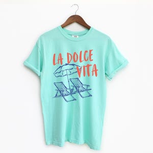 Island Reef Tee with the text LA DOLCE VITA across the chest.
Two sun chairs. One umbrella. Zero worries. Italy -where the espresso hits hard, the gelato never melts, and responsibility? Never heard of her.
Endless summer, featuring a dreamy graphic of striped beach bliss. Perfect for sun-chasers, rule-breakers, and anyone who believes naps are a lifestyle.
La Dolce Vita shirt, Tomato Girl summer, Limoncello, spaghetti vibes. Retro foodie, Portofino, Amalfi Coast Shirt, Sardines Tee