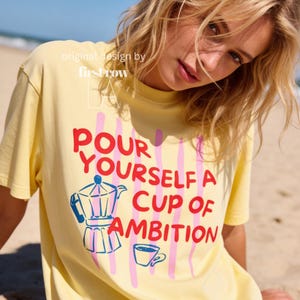 Woman wearing Dolly Parton "Pour Yourself a Cup of Ambition" Shirt, Retro Coffee Graphic, 9 to 5 Country Music Tee, Moka Pot, Coffee Club, Caffeine Lover.

Original desgin and copyright by first row LA.