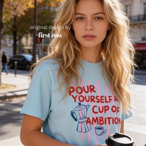 Woman wearing Dolly Parton "Pour Yourself a Cup of Ambition" Shirt, Retro Coffee Graphic, 9 to 5 Country Music Tee, Moka Pot, Coffee Club, Caffeine Lover.

Original desgin and copyright by first row LA.