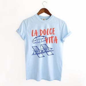 Chambray Light Blue Tee with the text LA DOLCE VITA across the chest.
Two sun chairs. One umbrella. Zero worries. Italy -where the espresso hits hard, the gelato never melts, and responsibility? Never heard of her.
Endless summer, featuring a dreamy graphic of striped beach bliss. Perfect for sun-chasers, rule-breakers, and anyone who believes naps are a lifestyle.
La Dolce Vita shirt, Tomato Girl summer, Limoncello, spaghetti vibes. Retro foodie, Portofino, Amalfi Coast Shirt, Sardines Tee