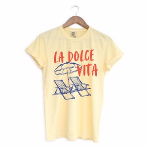 Butter Yellow Tee with the text LA DOLCE VITA across the chest.
Two sun chairs. One umbrella. Zero worries. Italy -where the espresso hits hard, the gelato never melts, and responsibility? Never heard of her.
Endless summer, featuring a dreamy graphic of striped beach bliss. Perfect for sun-chasers, rule-breakers, and anyone who believes naps are a lifestyle.
La Dolce Vita shirt, Tomato Girl summer, Limoncello, spaghetti vibes. Retro foodie, Portofino, Amalfi Coast Shirt, Sardines Tee