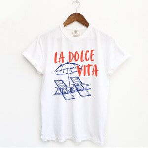White tee with the text LA DOLCE VITA across the chest.
Two sun chairs. One umbrella. Zero worries. Italy -where the espresso hits hard, the gelato never melts, and responsibility? Never heard of her.
Endless summer, featuring a dreamy graphic of striped beach bliss. Perfect for sun-chasers, rule-breakers, and anyone who believes naps are a lifestyle.
La Dolce Vita shirt, Tomato Girl summer, Limoncello, spaghetti vibes. Retro foodie, Portofino, Amalfi Coast Shirt, Sardines Tee