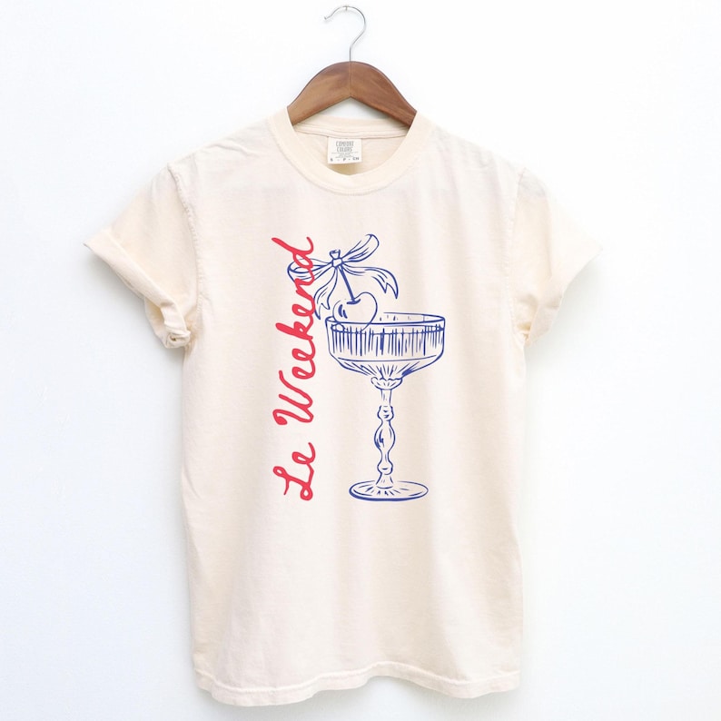 Ivory Beige T-shirt with the text Le Weekend and a Cherry Coquette Cocktail graphic.

Because what’s a good time without a little flair?

Perfect for brunch dates, rooftop soirées, or just channeling that effortlessly flirty energy. French twist, retro feel, full-on main character mood.
Weekend Shirt, Le Weekend, French T-Shirt, Weekending, Vintage Aesthetic, Coquette Bow Cherry, Cocktail Tee, y2k T-shirt, weekend vibes tee.