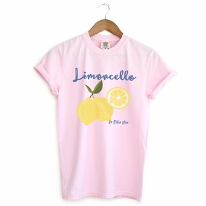 Blossom Light Pink T-shirt with the text Limoncello, La Dolce Vita, follewed by a juicy lemon graphics.
Limoncello Shirt, La Dolce Vita Tee, Lemon Shirt, Amalfi Coast, Italy TShirt, Vacay T-Shirt, Lemons Tee, Cocktail T Shirt, Retro Graphic Tee