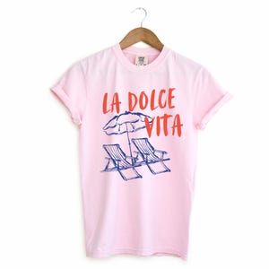 Blossom Light Pink Tee with the text LA DOLCE VITA across the chest.
Two sun chairs. One umbrella. Zero worries. Italy -where the espresso hits hard, the gelato never melts, and responsibility? Never heard of her.
Endless summer, featuring a dreamy graphic of striped beach bliss. Perfect for sun-chasers, rule-breakers, and anyone who believes naps are a lifestyle.
La Dolce Vita shirt, Tomato Girl summer, Limoncello, spaghetti vibes. Retro foodie, Portofino, Amalfi Coast Shirt, Sardines Tee