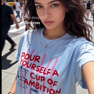 Woman wearing Dolly Parton "Pour Yourself a Cup of Ambition" Shirt, Retro Coffee Graphic, 9 to 5 Country Music Tee, Moka Pot, Coffee Club, Caffeine Lover.

Original desgin and copyright by first row LA.