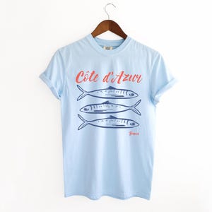 Chambray Light Blue T-shirt with the text Côtes d'Azur, France.

Côtes d'Azur France T-Shirt, Old Money Aesthetic, 3 Fish , French Riviera, Heritage, Sardines TShirt, France Travel Tee, Coastal Aesthetic, Retro Graphic Tee, French Vacation, Mediterranean