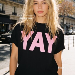 Woman wearing YAY T-Shirt, Happy Pink Graphic Tee, Cute Positive Shirt, Feel Good Tee, Fun Handwritten Statement Shirt, Dopamine shirt.

Original design and copyright by first row LA 2026.