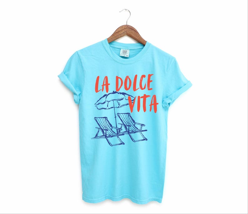 Lagoon Blue Tee with the text LA DOLCE VITA across the chest.
Two sun chairs. One umbrella. Zero worries. Italy -where the espresso hits hard, the gelato never melts, and responsibility? Never heard of her.
Endless summer, featuring a dreamy graphic of striped beach bliss. Perfect for sun-chasers, rule-breakers, and anyone who believes naps are a lifestyle.
La Dolce Vita shirt, Tomato Girl summer, Limoncello, spaghetti vibes. Retro foodie, Portofino, Amalfi Coast Shirt, Sardines Tee