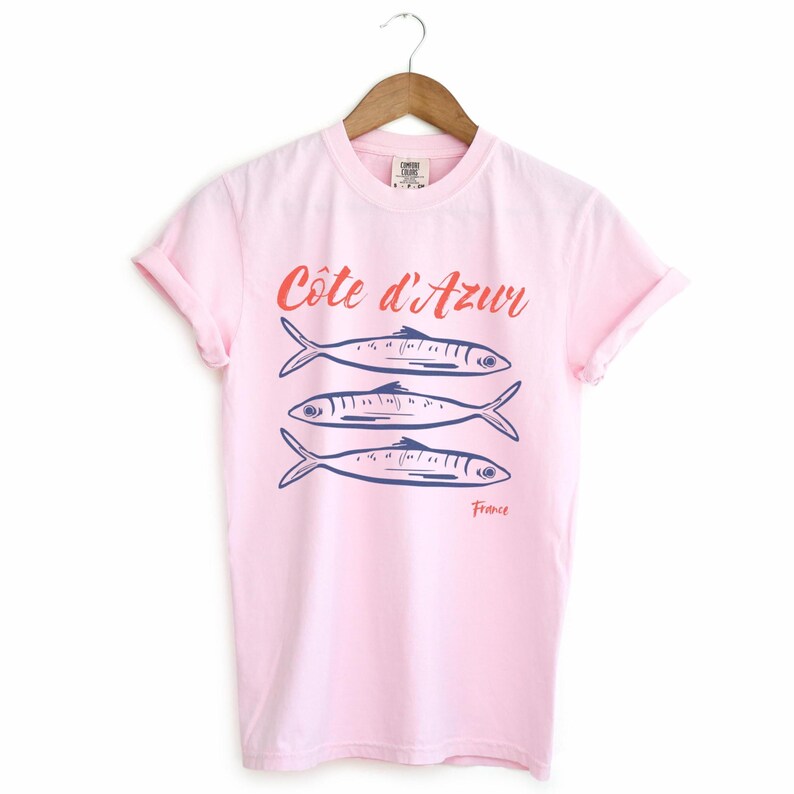 Blossom Light Pink T-shirt with the text Côtes d'Azur, France.

Côtes d'Azur France T-Shirt, Old Money Aesthetic, 3 Fish , French Riviera, Heritage, Sardines TShirt, France Travel Tee, Coastal Aesthetic, Retro Graphic Tee, French Vacation, Mediterranean