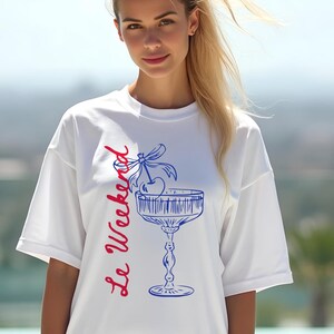 Model wearing a white T-shirt with the text Le Weekend and a Cherry Coquette Cocktail graphic.

Because what’s a good time without a little flair?

Perfect for brunch dates, rooftop soirées, or just channeling that effortlessly flirty energy. French twist, retro feel, full-on main character mood.
Weekend Shirt, Le Weekend, French T-Shirt, Weekending, Vintage Aesthetic, Coquette Bow Cherry, Cocktail Tee, y2k T-shirt, weekend vibes tee.
