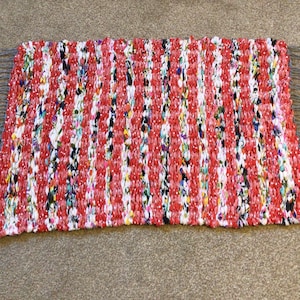 May include: A red, white and blue braided rug with fringe. The rug is made from recycled materials and has a colourful, textured design.