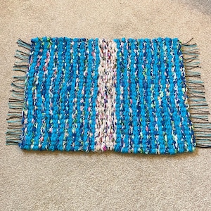 May include: A blue and white woven rug with fringe on the edges. The rug has a vertical stripe of white fabric in the centre.