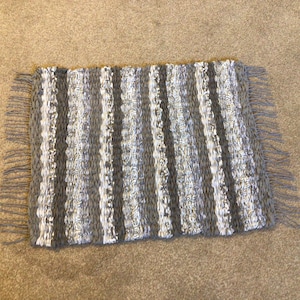 May include: A grey and white striped woven rug with fringe on all sides.