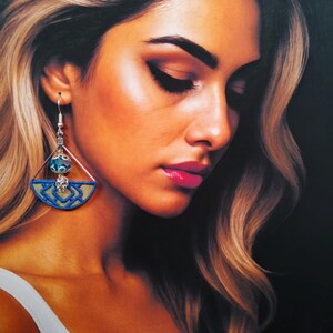 May include: A pair of silver earrings with a blue and gold geometric design. The earrings feature a teardrop-shaped blue gemstone and a dangling charm.