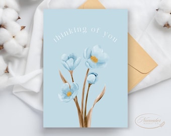 Könnte beinhalten: Eine hellblaue Karte mit dem Text "Thinking of you" in weißen Buchstaben. Die Karte zeigt eine Aquarell-Illustration von blauen Blumen mit braunen Stielen.