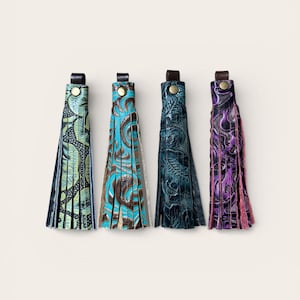 May include: Four leather tassels in a row, each with a different colour and pattern. The colours include green, turquoise, dark teal, and purple. Each tassel has a leather loop and a metal button.