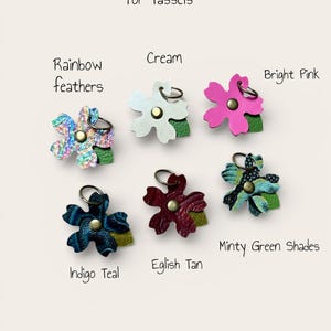 May include: Blossom charms for tassels in a range of colours. The charms include Rainbow Feathers, Cream, Bright Pink, Indigo Teal, Eglish Tan, and Minty Green Shades. Each charm is flower-shaped with a metal ring.