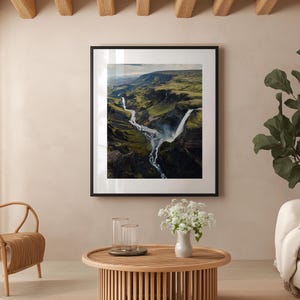 Pu&ograve; includere: Fotografia incorniciata di una cascata in un canyon verde e marrone. L'immagine &egrave; esposta in un soggiorno con un tavolino in legno, sedie in vimini e un divano bianco. La stanza ha una combinazione di colori neutri.